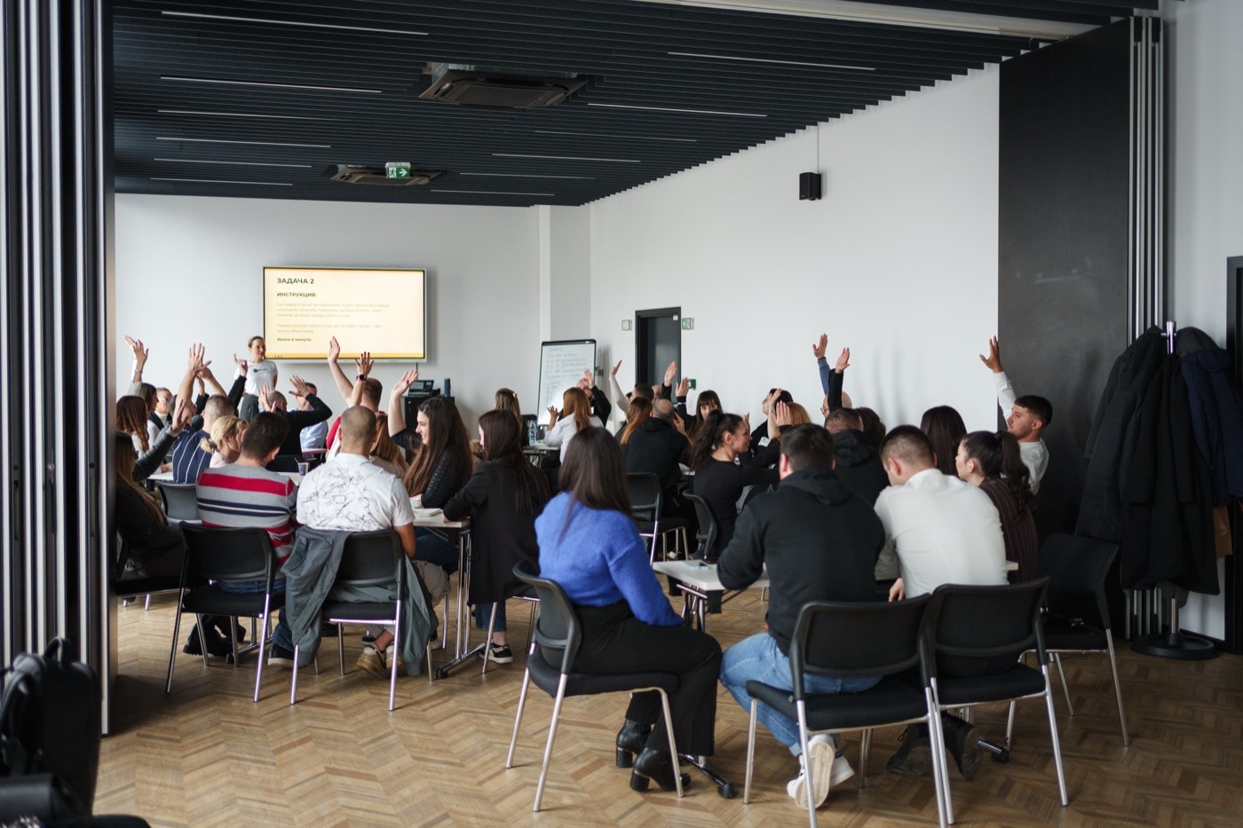 A room of participants with their hands raised towards the facilitator during a session